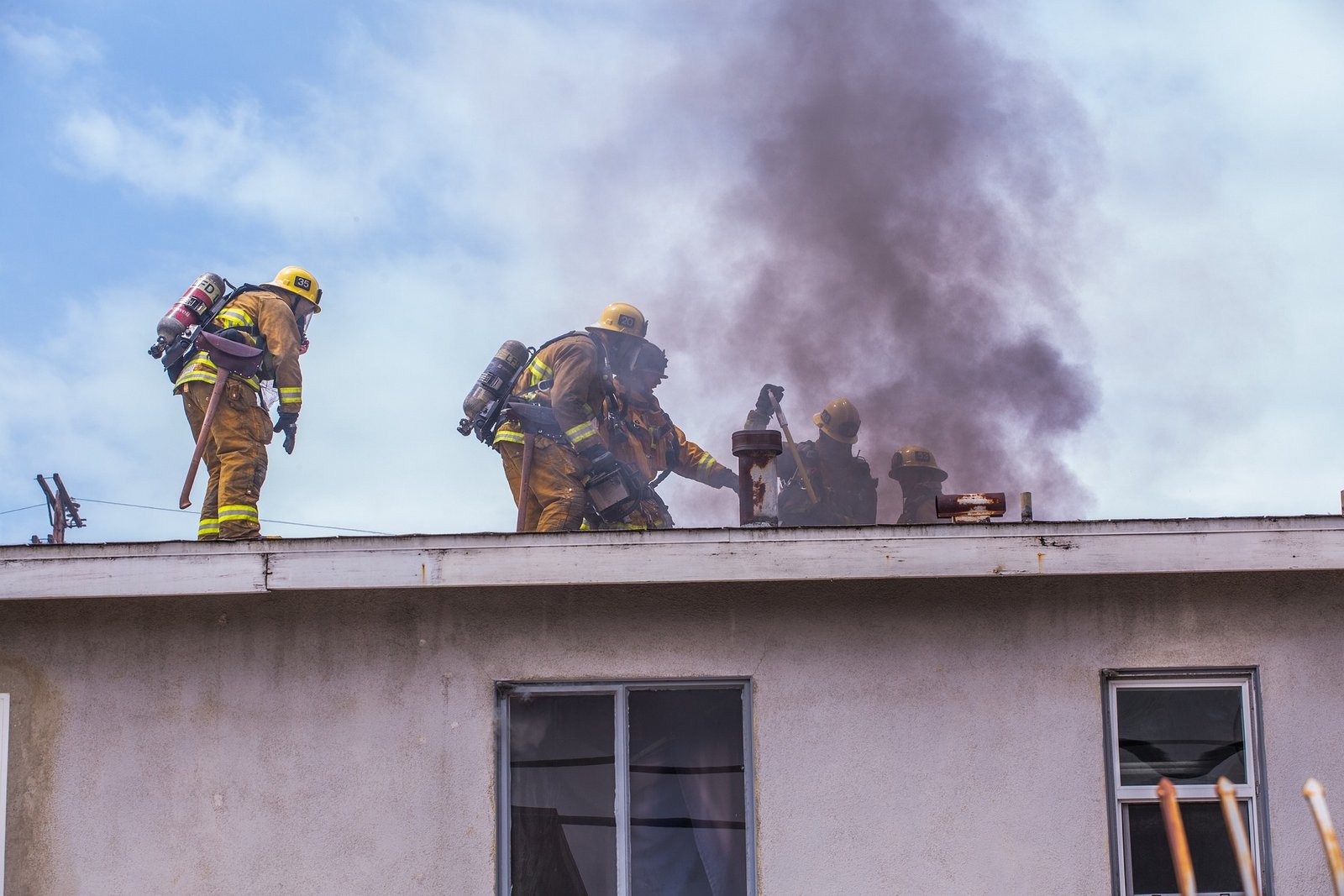 Firefighters controlling house fire on roof with smoke rising